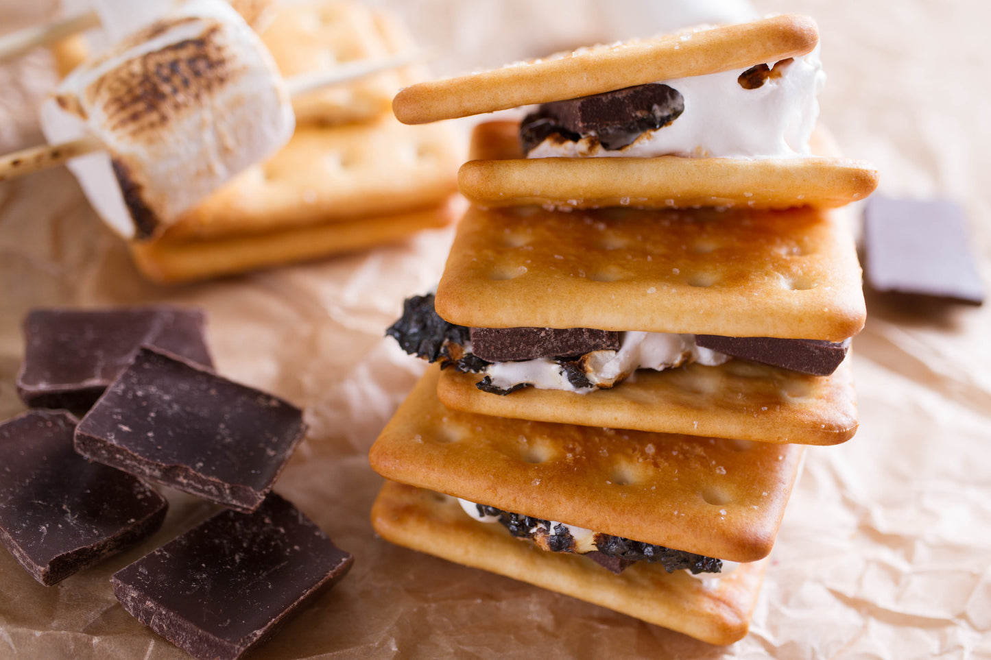 Stack of s'mores with graham crackers, marshmallows, and chocolate on a textured surface.