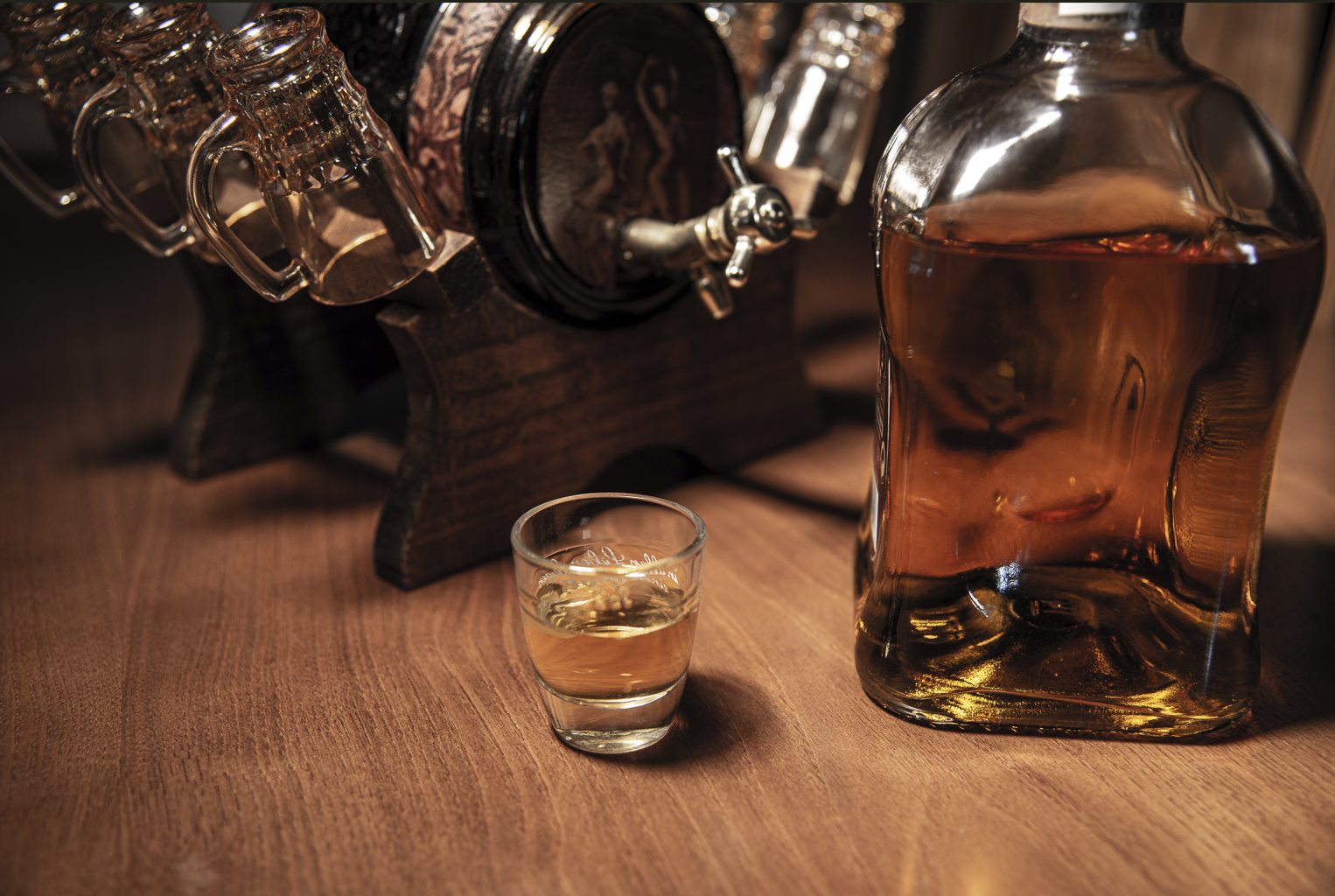 Whiskey bottle and shot glass on a wooden surface with a bar setup in the background.