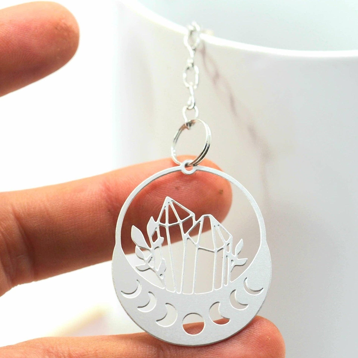 Silver pendant with crystal design held in a hand against a white background