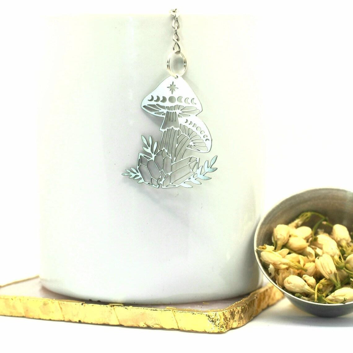 Silver mushroom pendant on a white cup with a bowl of dried flowers on a white background